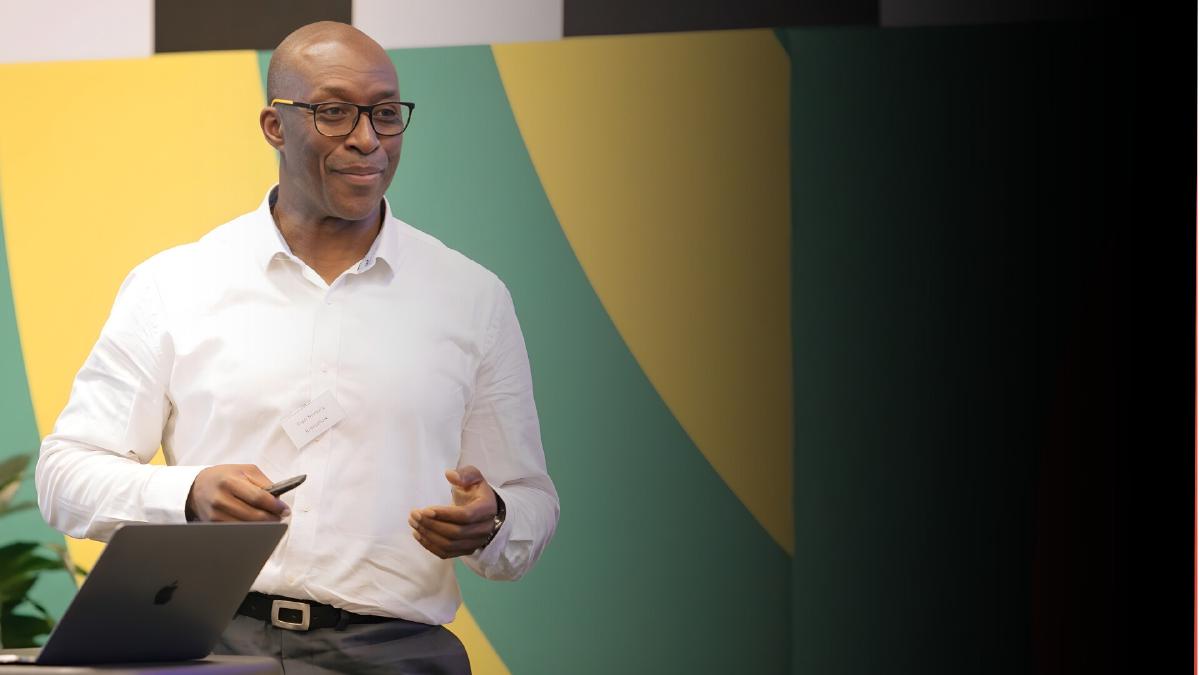 Fredi Nonyelu speaking at a conference, holding a microphone on stage